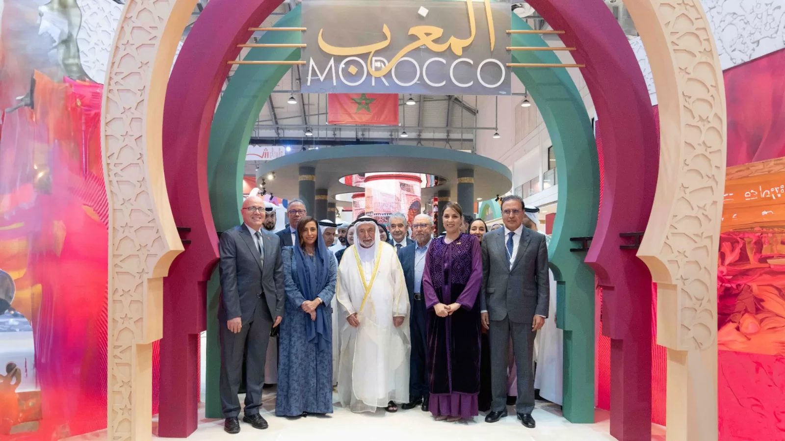 Dignitaries pose beneath a colorful Morocco arch at an indoor cultural exhibition.