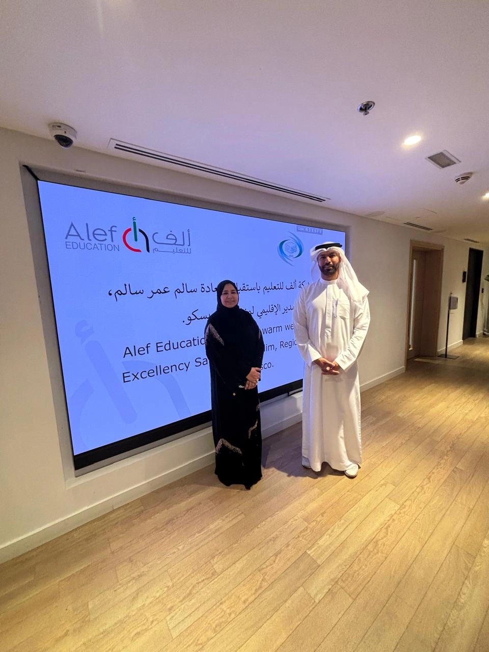 A man in a kandura and a woman in an abaya stand before an Alef Education and ICESCO welcome screen.