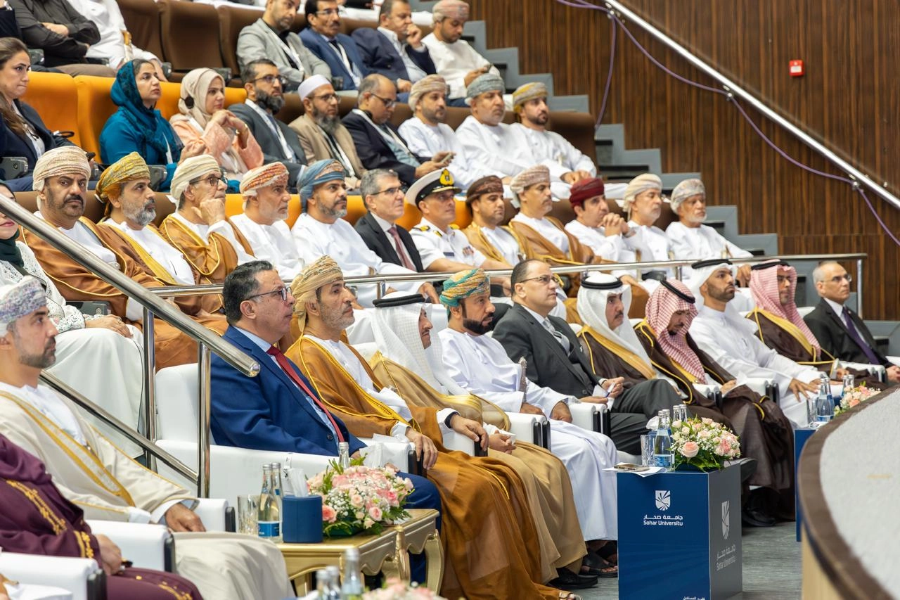 Dignitaries in Omani and Emirati dress sit in white chairs beside a Sohar University logo pedestal.