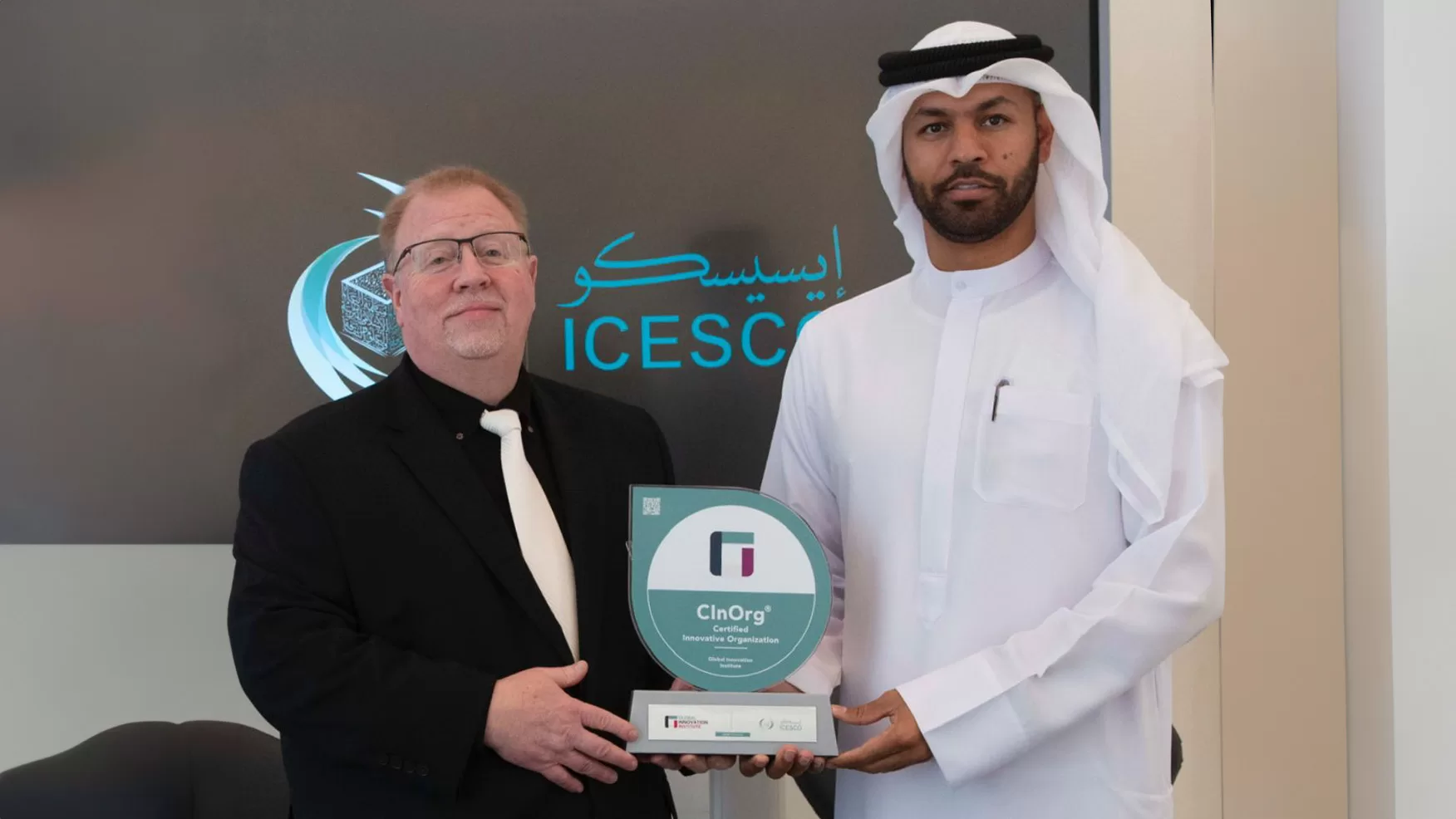 Two men hold a circular Certified Innovative Organization award before an ICESCO branded screen.