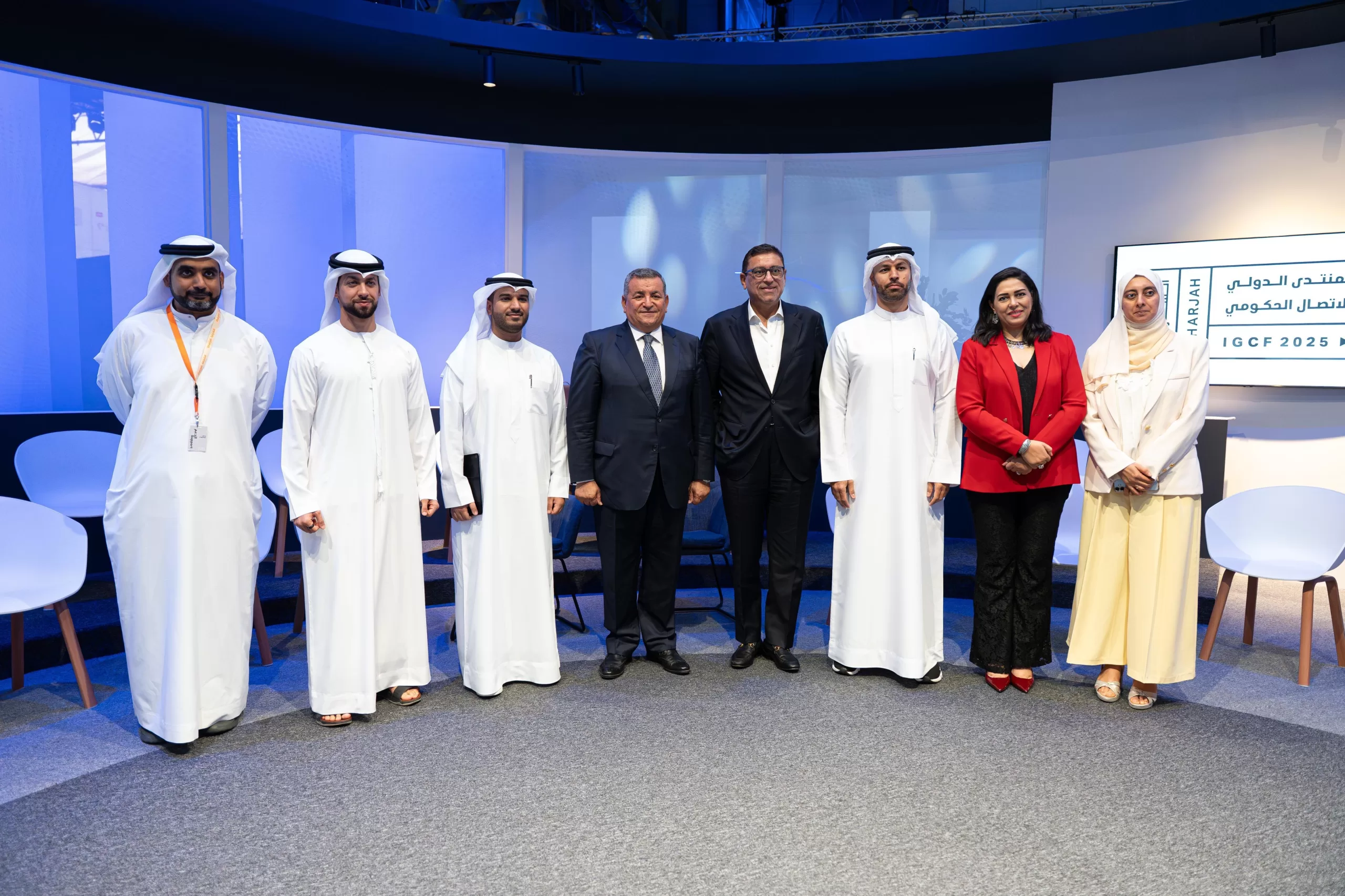 Eight officials in Emirati dress and business attire pose on stage before an IGCF 2025 Sharjah screen.