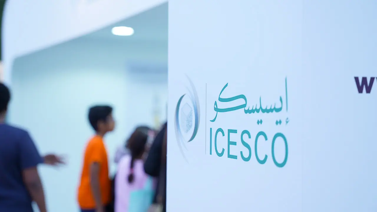 ICESCO teal logo on a white wall with blurred event hall interior