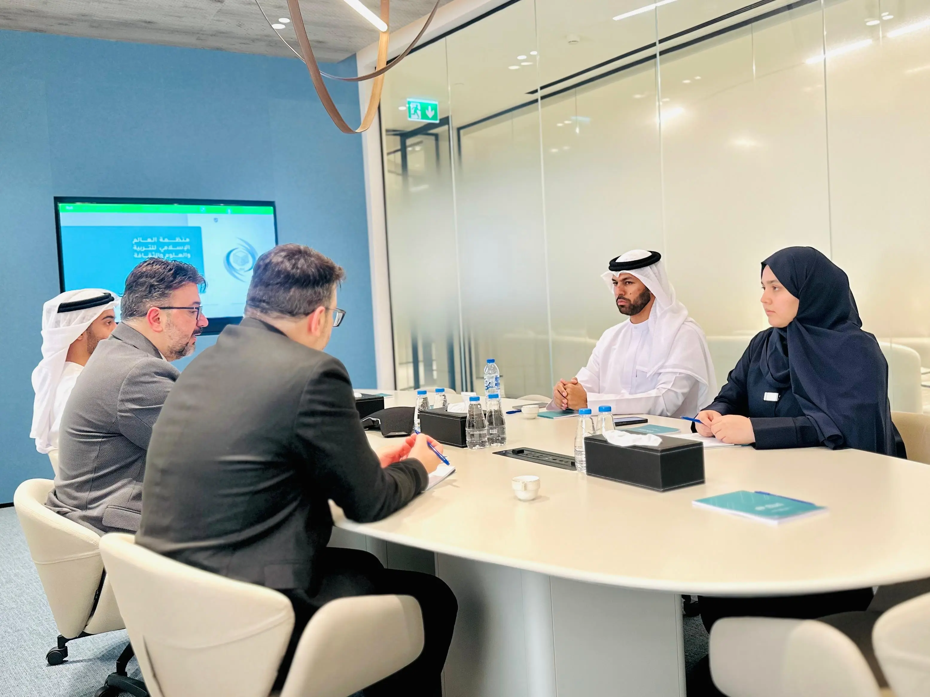 Professionals in Emirati and business attire meet around a table with an ICESCO slide on screen.