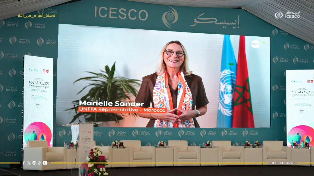 Stage screen shows UNFPA Representative Marielle Sander beside empty white chairs and Families conference banners.