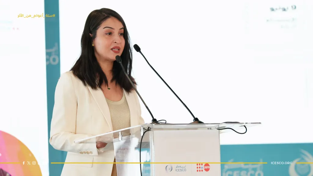 A woman in a white blazer speaks at a clear podium displaying ICESCO and UNFPA logos.