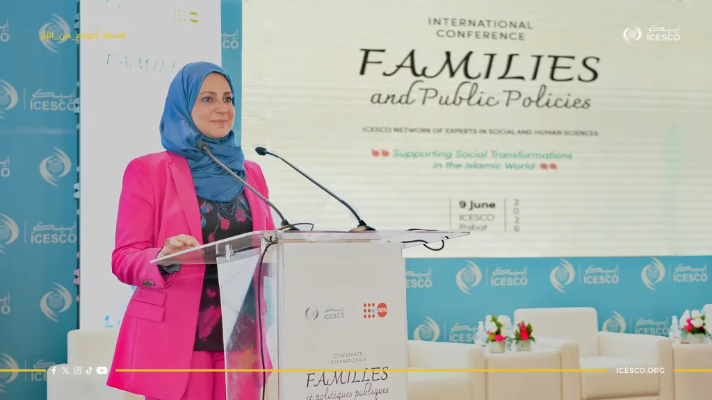 A woman in a pink blazer and blue hijab speaks at the Families and Public Policies conference podium.